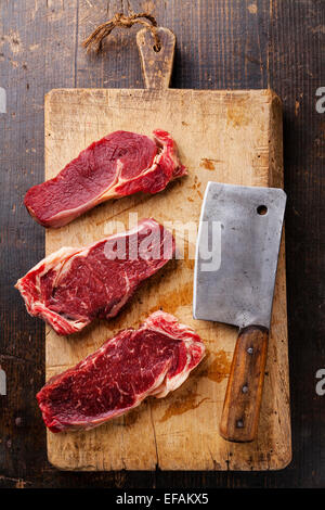 Materie carni fresche Ribeye entrecote e carne cleaver sul bordo di taglio su sfondo di legno Foto Stock