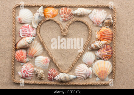 Cuore simbolico realizzato dalla corda e conchiglie di mare distesi sulla sabbia, come sfondo Foto Stock