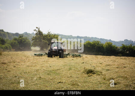 Il trattore e il voltafieno fieno svolta nel campo, Oxfordshire, Inghilterra Foto Stock