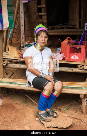 Giovani birmani tribù Karen lungo collo donna con collo anelli, un rifugiato birmano, seduti al di fuori di una capanna di fango in Karen Padong village, Chiang Rai, Thailandia Foto Stock