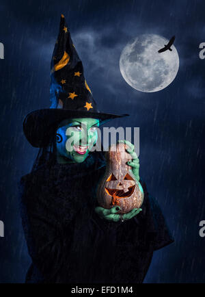 Strega con pelle verde azienda scolpito zucca di Halloween a luna e cielo scuro con sensore pioggia Foto Stock