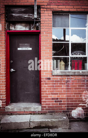 Una porta ed una finestra su un edificio di mattoni rossi con un cemento stoop che conduce alla porta, e aperto un segno. Foto Stock