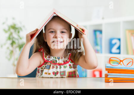 Preschooler bambino ragazza con libro sopra la testa Foto Stock