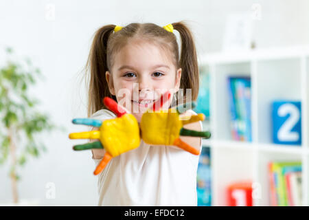 Bambina con le mani di vernice su sfondo di vivaio Foto Stock