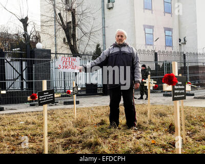 Croci poste dagli attivisti e recanti i nomi di 30 persone che sono morte nel bombardamento in Mariupol su Jan, 24 sono visibili in primo piano un uomo con un banner "Putin, ottenere al di fuori dell'Ucraina." Il sig. vicino all'Ambasciata russa a Kiev, Ucraina, Domenica, 1 febbraio 2015. Foto Stock