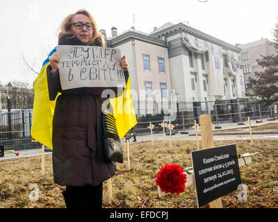 Croci poste dagli attivisti e recanti i nomi di 30 persone che sono morte nel bombardamento in Mariupol su Jan, 24 sono visti in primo piano come donna in piedi con un banner "Putler - №1 attentati nel mondo" vicino all'Ambasciata russa a Kiev, Ucraina, Domenica, 1 febbraio 2015. Foto Stock