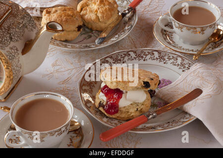 Una tabella per inglese tradizionale tè alla crema. Inceppamento e scones illuminato naturalmente con una tovaglia e belle cina Foto Stock