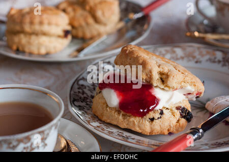 Una tabella per inglese tradizionale tè alla crema. Inceppamento e scones illuminato naturalmente con una tovaglia e belle cina Foto Stock