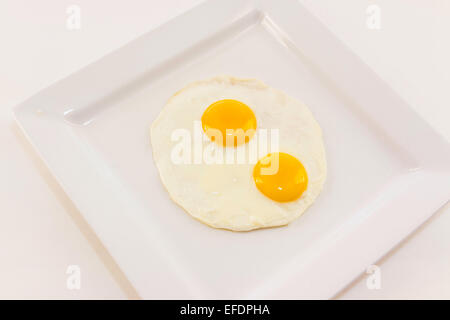 Due uova fritte su un quadrato piastra bianca su sfondo bianco Foto Stock