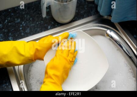 Una donna lavando pentole giallo da indossare guanti di gomma Foto Stock