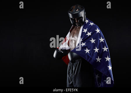 Ritratto di giovane maschio boxer con la bandiera americana su sfondo nero. L'uomo africano nella boxe marcia guardando verso il basso. Foto Stock