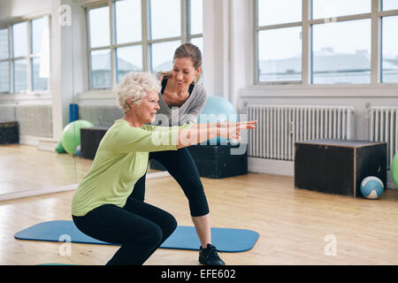 Donna anziana fare esercizio con il suo personal trainer presso la palestra. Istruttore di palestra assistere senior donna nel suo allenamento. Foto Stock