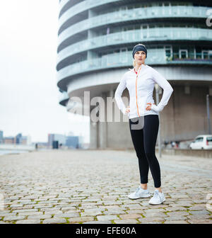 Lunghezza completa immagine di montare la giovane donna in abbigliamento sportivo permanente sulla strada guardando lontano. Fiducioso atleta femminile su outdoor training Foto Stock