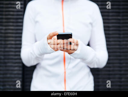 Primo piano della giovane donna prendendo una pausa forma allenamento tramite telefono cellulare. Focus su mani e smart phone. Foto Stock