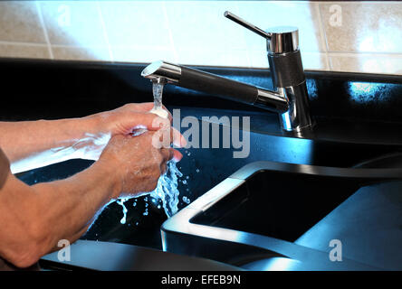Un uomo è visto lavarsi le mani sotto un rubinetto di cucina . L'immagine è sotto accesa per mostrare i dettagli in acqua Foto Stock
