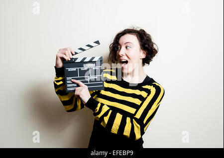 Ragazza in giallo t-shirt con la faccia buffa che mostra filmato battaglio su sfondo bianco Foto Stock