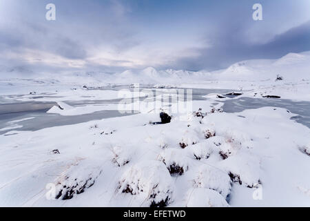 Un parzialmente congelati Lochan na Stainge con le montagne coperte di neve del Monte Nero dietro Foto Stock