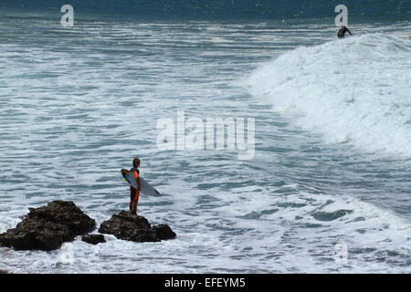 Un giovane maschio surfer sorge su rocce la scansione del surf a Sandon Point, Bulli, Nuovo Galles del Sud, Australia. Foto Stock