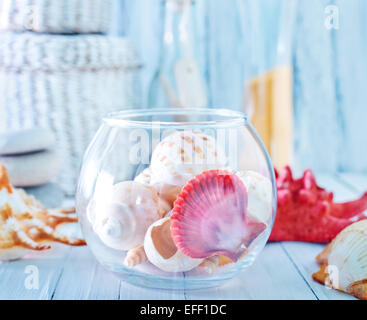 Conchiglie di mare in recipiente di vetro e su un tavolo Foto Stock