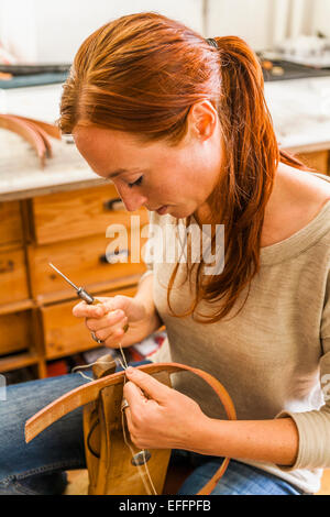 Donna di cucitura del tessuto elastico rubber band utilizzando i lacci pony e awl Foto Stock