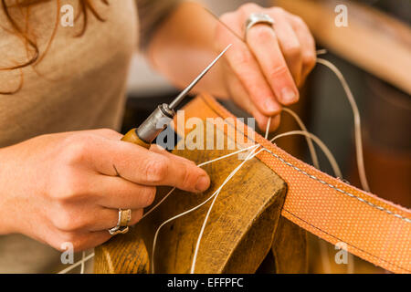 Donna di cucitura del tessuto elastico rubber band utilizzando i lacci pony e awl Foto Stock