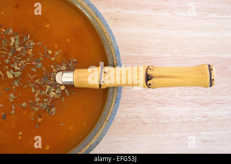 Vista ravvicinata di una ciotola di pomodoro bisque zuppa con erbe di menta il condimento e un cucchiaio su una tavola di legno. Foto Stock