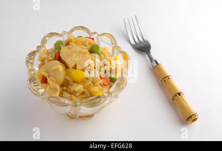 Una piccola ciotola di vetro di pollo con verdure in una salsa di ananas su un tavolo bianco con una forcella a lato Foto Stock
