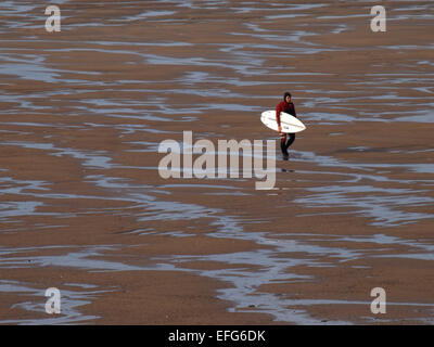 Lone surfer tornare indietro a piedi su una spiaggia deserta dal mare dopo la navigazione su una giornata invernale e, Widemouth Bay, Bude Cornwall, Regno Unito Foto Stock