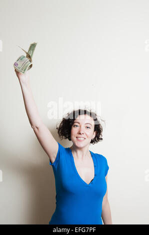 Giovane donna graziosa con il blu t-shirt casual felice mentre mostrando dollari up braccio su sfondo bianco Foto Stock