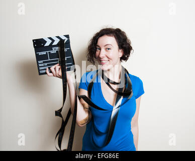 Giovane donna graziosa con il blu t-shirt casual e filmina intorno al collo è sorridente, tenendo un filmato battaglio su sfondo bianco Foto Stock