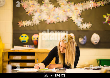 Una ragazza adolescente di lavoro e di scrivere i suoi corsi in un anno 13 classe d'arte in una scuola secondaria, Wales UK Foto Stock