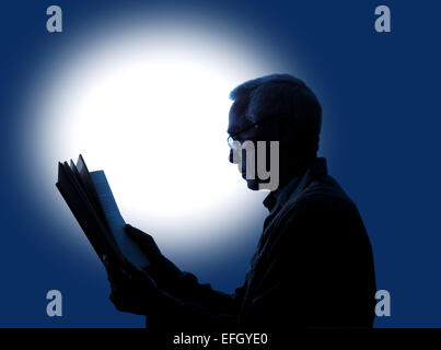 Una macchia di lt sfondo dando un effetto di silhouette di un uomo di circa sessanta anni la lettura di un libro mentre indossa gli occhiali da lettura Foto Stock