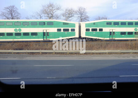 Un Canadese double deck treni passeggeri che viaggiano parallelamente a un'autostrada. Foto Stock