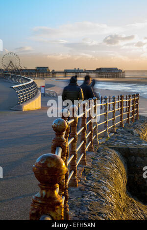 I visitatori del Resort vicino al vecchio ringhiere in ghisa guardando il sole di setting, sul lungomare di Blackpool, Lancashire, Regno Unito Foto Stock