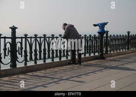 Uomo in piedi vicino al telescopio blu guardando verso il basso dal punto di vista sul mare, in Tarragona Catalogna Foto Stock