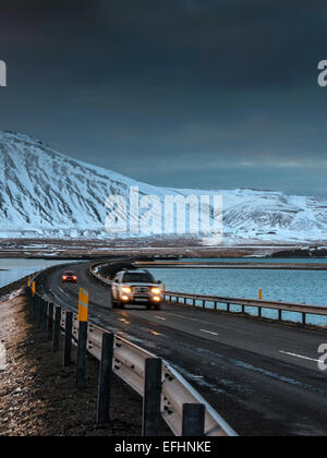 Due veicoli attraversano il islandese causeway a Kolgrafafjorour, con fari accesi. Foto Stock