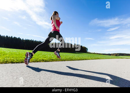 Donna jogging lungo una strada, Munsing, Baviera, Germania Foto Stock