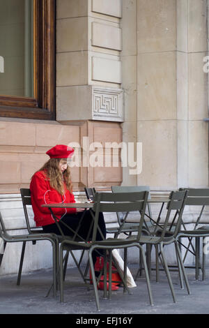 Signora in rosso seduto da solo Foto Stock