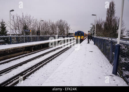 In treno Arrivando in treno suburbano station coperto di neve di luce, Hampton Wick, Surrey, England, Regno Unito Foto Stock