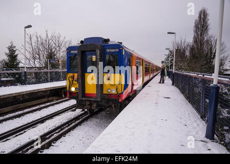 In treno Arrivando in treno suburbano station coperto di neve di luce, Hampton Wick, Surrey, England, Regno Unito Foto Stock