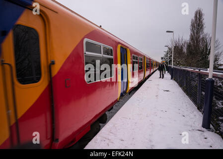 In treno Arrivando in treno suburbano station coperto di neve di luce, Hampton Wick, Surrey, England, Regno Unito Foto Stock