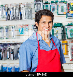 Bello il lavoratore nel grembiule rosso sorridente al negozio di hardware Foto Stock