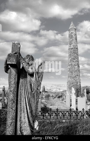 Angelo statua prima di una antica torre rotonda e celtic cimitero con cattedrale di Ardmore nella contea di Waterford, Irlanda Foto Stock