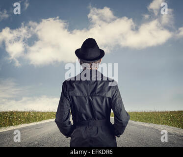 Man in black hat su strada a blu cielo nuvoloso sfondo Foto Stock