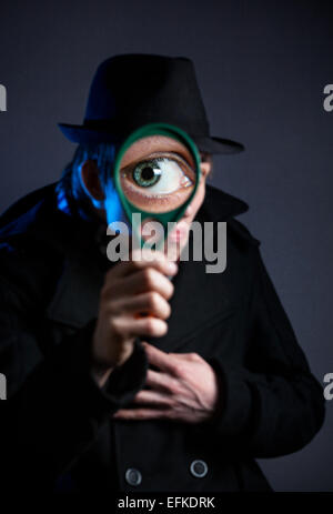 Man in black hat con lente di ingrandimento in vetro scuro dello sfondo Foto Stock