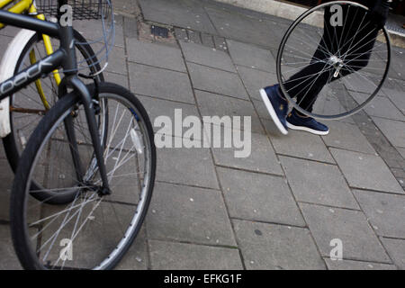 Una persona che porta una ruota di bicicletta, meno del proprio pneumatico, passato bloccato le bici in centro a Londra. Foto Stock