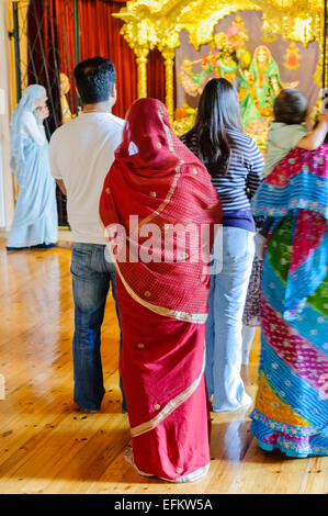 Hare Krishna devoti stand a pregare e celebrare nella parte anteriore di un altare in un tempio di camera. Foto Stock