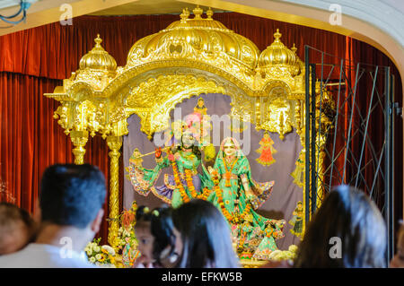 Hare Krishna devoti stand a pregare e celebrare nella parte anteriore di un altare in un tempio di camera. Foto Stock