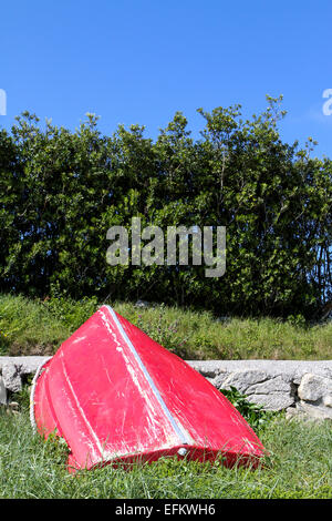 Rosso capovolta barca a remi appoggiata contro il sentiero, isole Scilly, Regno Unito Foto Stock