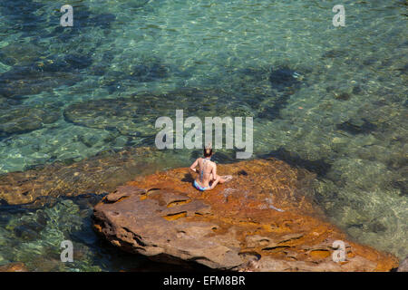 Donna seduta su una roccia a Gordon's Bay, Sydney, Australia Foto Stock